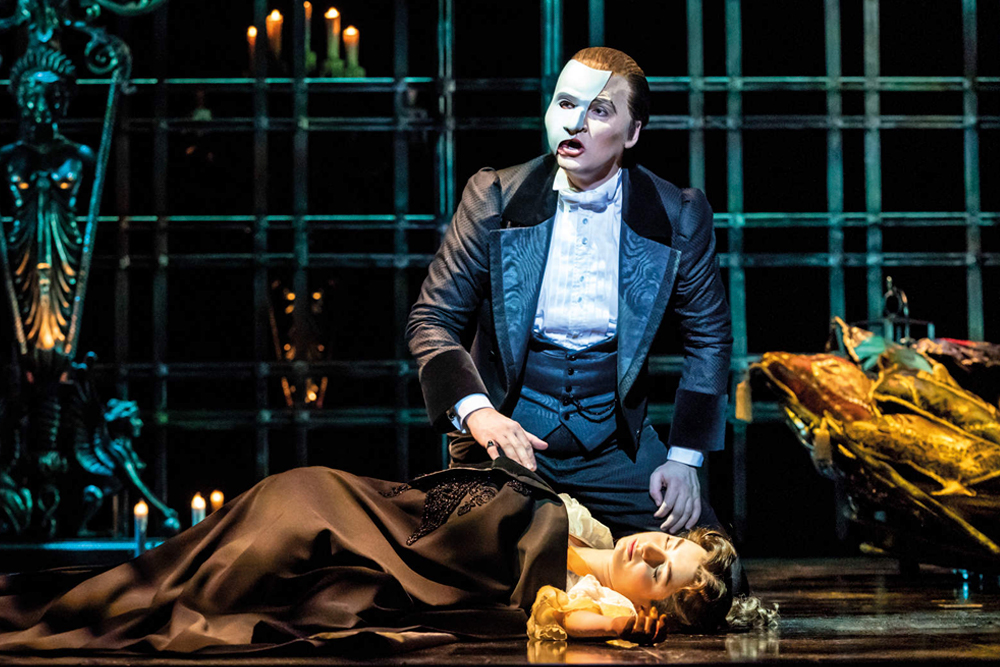 Billet pour le spectacle Le Fantôme de l'Opéra à Londres - Plongez dans le monde enchanteur du Fantôme de l'Opéra au théâtre historique de Londres, le Théâtre de Sa Majesté, où drame et musique se rejoignent pour une expérience live véritablement inoubliable. Dès que le rideau se lève, vous serez entraîné dans l'histoire poignante de Christine, une jeune chanteuse à la voix d'or, et du mystérieux Fantôme qui vit sous l'opéra. Son masque sombre et sa tanière secrète ajoutent une atmosphère de mystère, tandis que son amour profond pour Christine donne lieu à des moments de passion, de tension et de peine sur scène. Admirez les décors époustouflants qui transforment le théâtre en grand halls d'opéra, passages secrets et une tanière souterraine éclairée à la bougie. Les costumes somptueux — robes flottantes, smokings élégants et la cape emblématique du Fantôme — donnent vie aux personnages en couleurs vives. Alors que l'orchestre live emplit la salle de la partition envoûtante d'Andrew Lloyd Webber, vous entendrez des chansons célèbres comme La Musique de la Nuit, Tout ce que je te demande et Pense à moi, chacune interprétée avec une émotion puissante par des chanteurs de classe mondiale. Les effets spéciaux ajoutent une magie supplémentaire : des bougies vacillent sur le lustre du Fantôme, des pétales de rose rouges flottent dans l'air et des ombres dansent sur les murs, créant une atmosphère de romance et de suspense. Chaque instant est conçu pour captiver vos sens, des scènes calmes et tendres aux crescendo palpitants qui feront battre votre cœur. Billet pour le spectacle Le Fantôme de l'Opéra à Londres - Image 1 sur 5