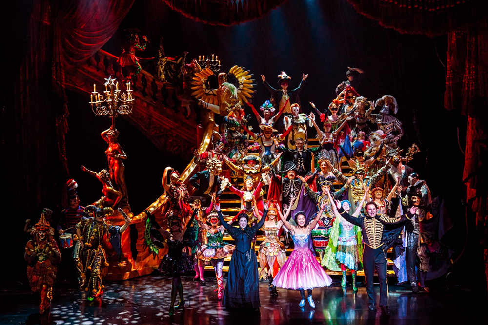 Billet pour le spectacle Le Fantôme de l'Opéra à Londres - Plongez dans le monde enchanteur du Fantôme de l'Opéra au théâtre historique de Londres, le Théâtre de Sa Majesté, où drame et musique se rejoignent pour une expérience live véritablement inoubliable. Dès que le rideau se lève, vous serez entraîné dans l'histoire poignante de Christine, une jeune chanteuse à la voix d'or, et du mystérieux Fantôme qui vit sous l'opéra. Son masque sombre et sa tanière secrète ajoutent une atmosphère de mystère, tandis que son amour profond pour Christine donne lieu à des moments de passion, de tension et de peine sur scène. Admirez les décors époustouflants qui transforment le théâtre en grand halls d'opéra, passages secrets et une tanière souterraine éclairée à la bougie. Les costumes somptueux — robes flottantes, smokings élégants et la cape emblématique du Fantôme — donnent vie aux personnages en couleurs vives. Alors que l'orchestre live emplit la salle de la partition envoûtante d'Andrew Lloyd Webber, vous entendrez des chansons célèbres comme La Musique de la Nuit, Tout ce que je te demande et Pense à moi, chacune interprétée avec une émotion puissante par des chanteurs de classe mondiale. Les effets spéciaux ajoutent une magie supplémentaire : des bougies vacillent sur le lustre du Fantôme, des pétales de rose rouges flottent dans l'air et des ombres dansent sur les murs, créant une atmosphère de romance et de suspense. Chaque instant est conçu pour captiver vos sens, des scènes calmes et tendres aux crescendo palpitants qui feront battre votre cœur. Billet pour le spectacle Le Fantôme de l'Opéra à Londres - Image 2 sur 5